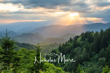 Sun rays illuminate lush green mountains under a cloudy sky.