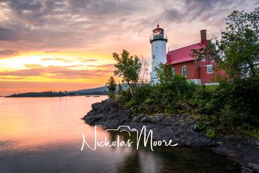Lighthouse on rocky shore during a vibrant sunset.