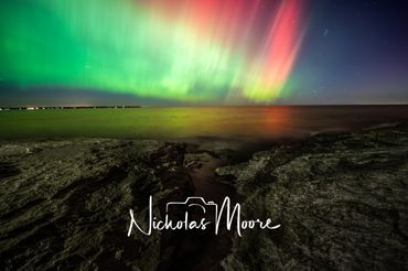 Vibrant northern lights shimmer over a rocky shoreline at night.