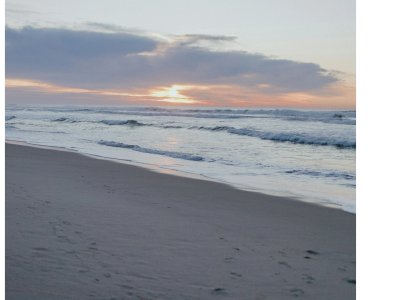 Sunset over a sandy beach with gentle waves.