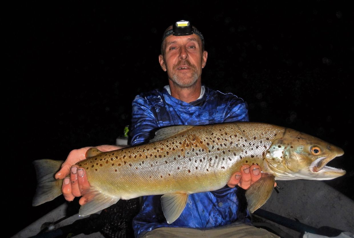 Man holding a large fish at night with a headlamp.