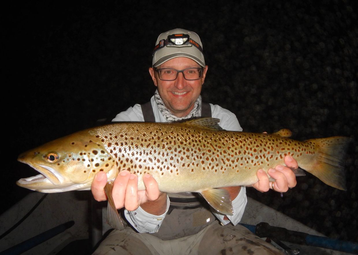 Man proudly holding a large brown trout he caught at night.