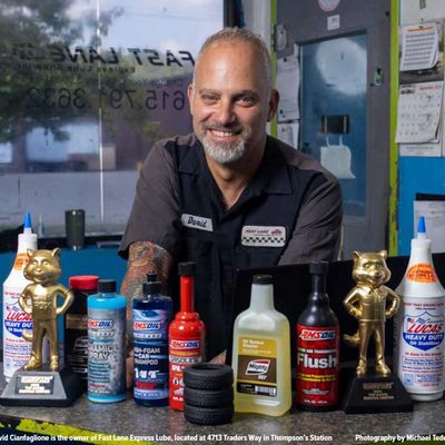 Man smiling behind a collection of automotive products and golden trophies.