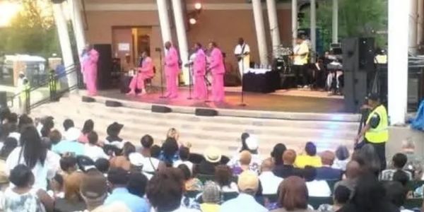 A band dressed in pink performs on an outdoor stage to a seated audience.