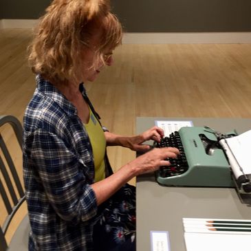 A woman typing on a vintage typewriter at a table indoors.