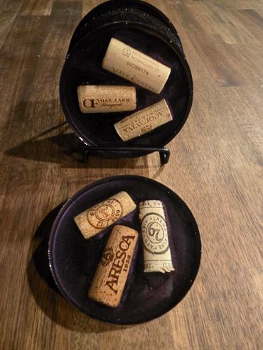 Two black dishes holding six wine corks on a wooden surface.