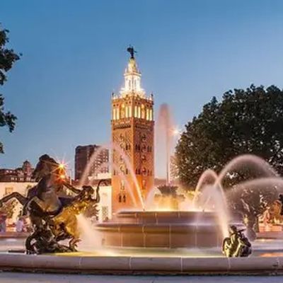 Fountain with water jets and a tall clock tower at dusk.