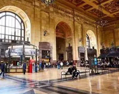 Spacious historic train station interior with high arched windows and wooden benches.