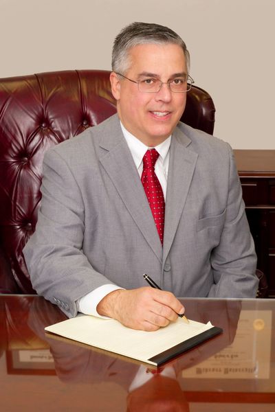 Attorney Pavlack writing on a notepad with a pen and sitting at a table smiling. 