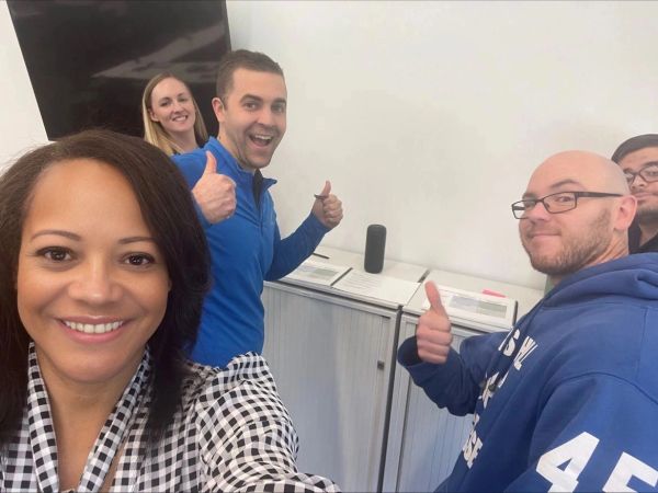 A group of five people smiling and giving thumbs up indoors.