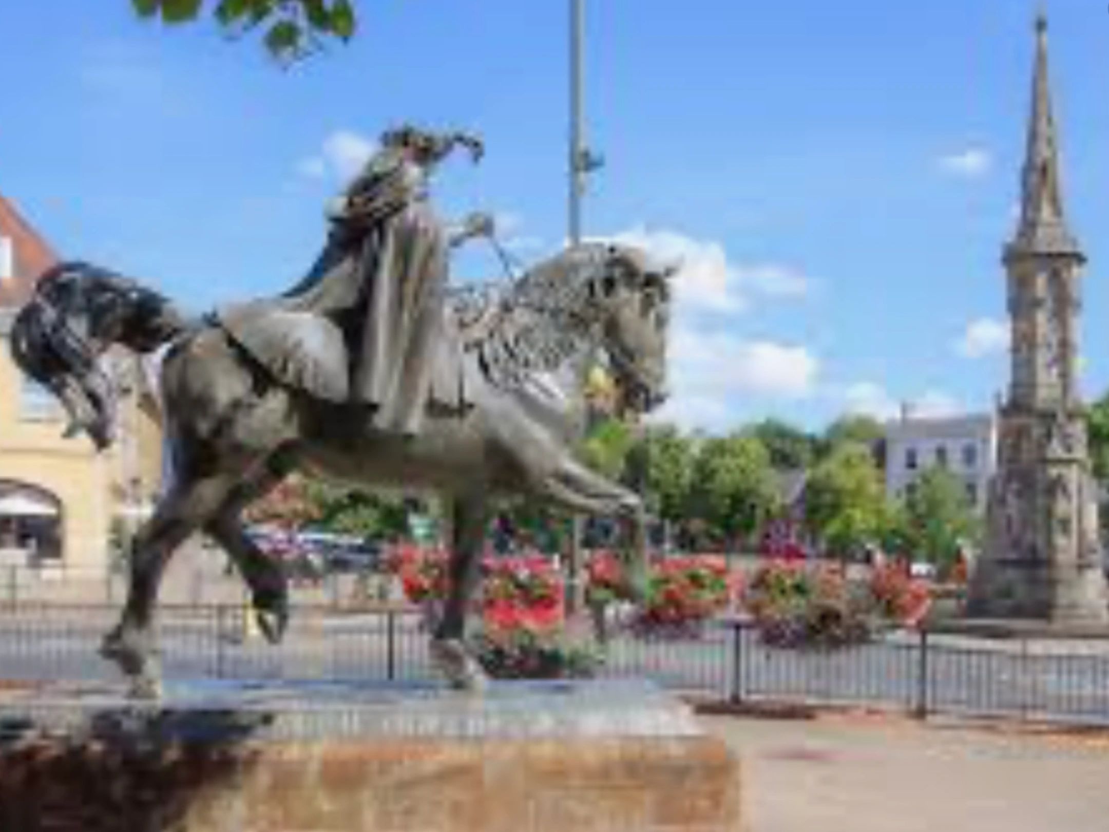 Statue of a rider on a rearing horse in a sunny town square with flowers.