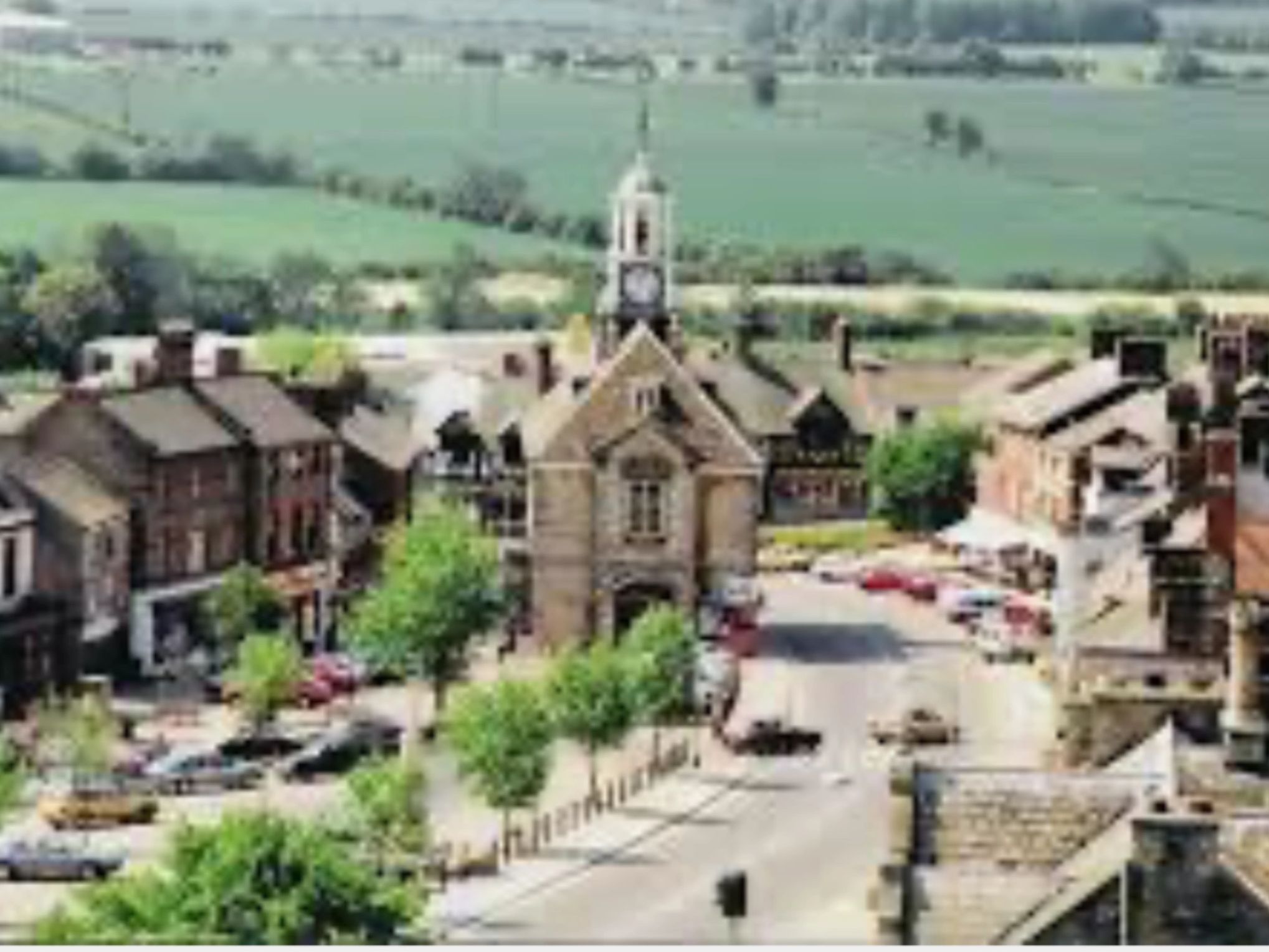 A small town with a clock tower and green fields in the background.