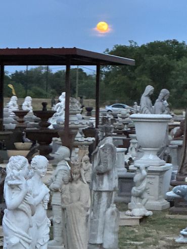 Outdoor display of various stone statues and sculptures under a dusk sky.