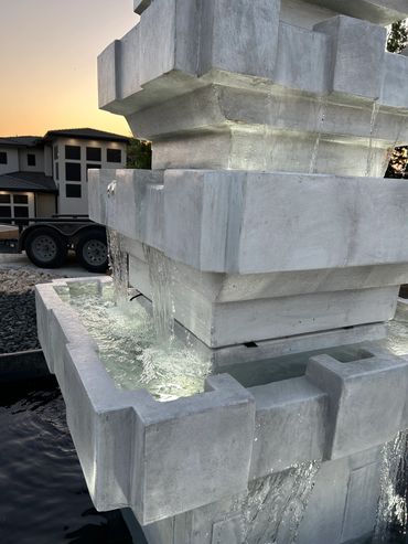 Modern geometric concrete water fountain with cascading water at sunset.