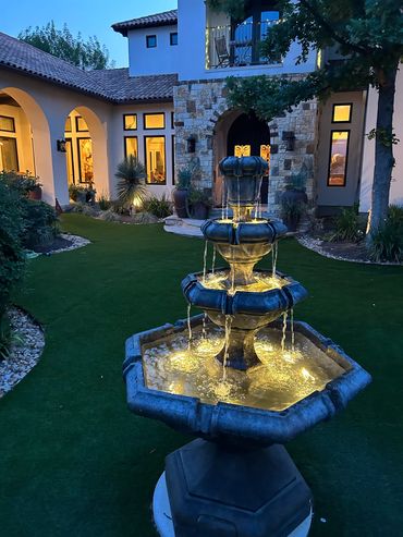 Illuminated three-tier water fountain in a beautiful courtyard at dusk.