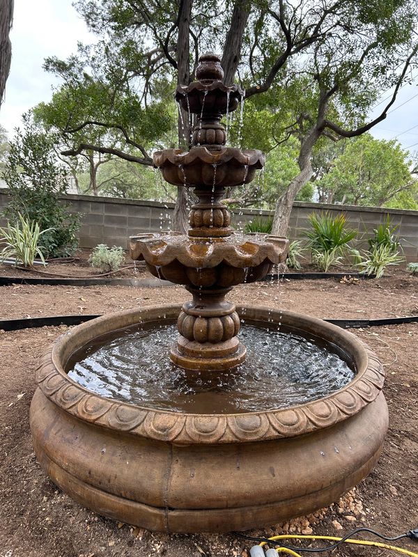 Three-tiered stone water fountain in a garden setting.