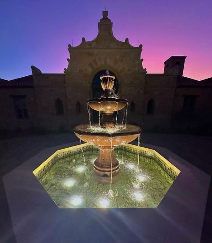 Illuminated tiered water fountain at twilight in front of historic building.