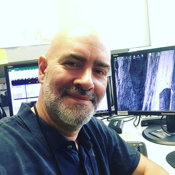 Man with a beard smiling at the camera at his office desk.