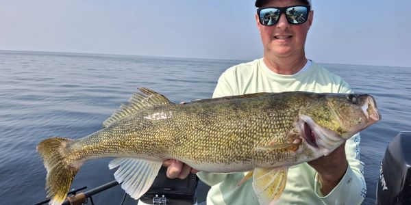 Man on a boat proudly holding a large fish he caught.