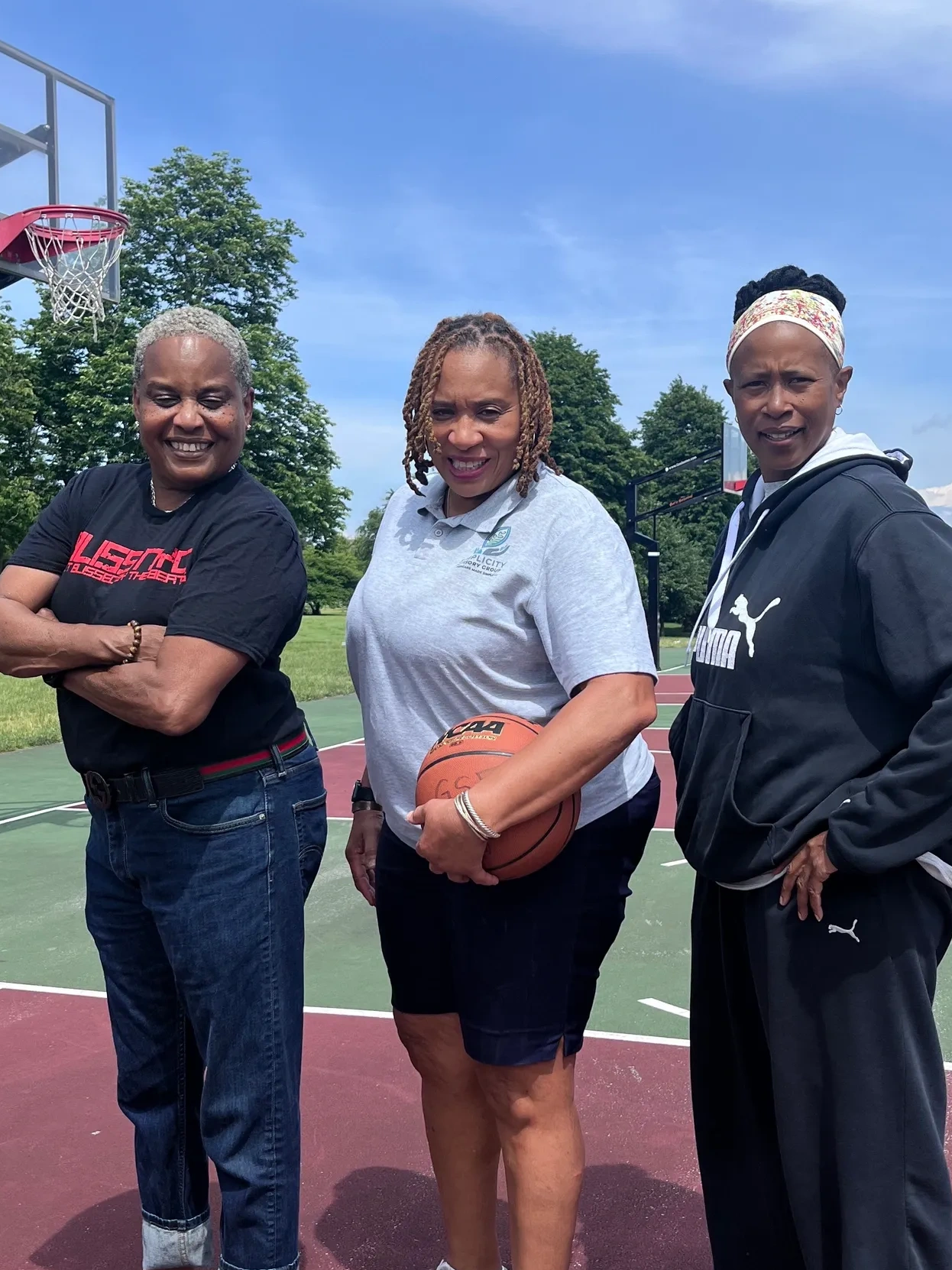 Three women posing on a basketball court, one holding a basketball.