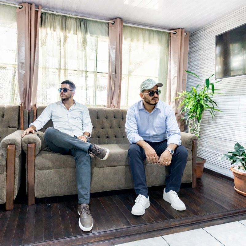 an office worker sitting next to his friend nonchalantly on a sofa in the living room of the house