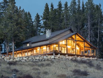 Modern cabin with warm lighting nestled in a forested hillside at dusk.