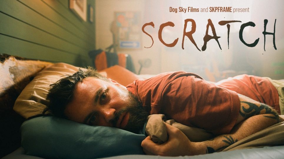 Man with a beard lies on bed, staring ahead under the title 'SCRATCH'.