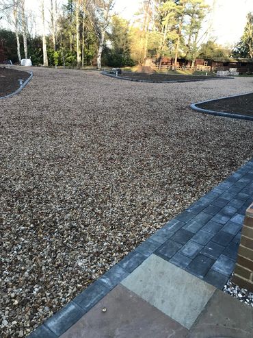 Newly laid gravel driveway with paved edges and surrounding garden beds.