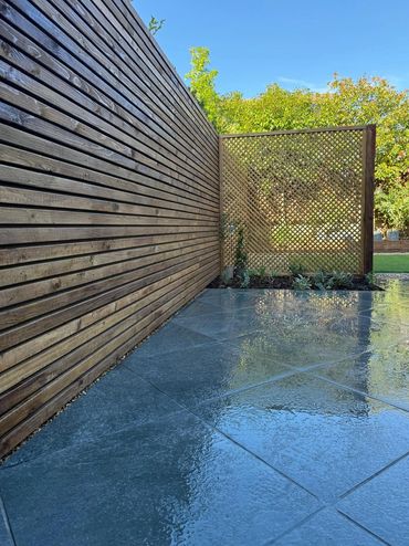Modern backyard with wet stone tiles and wooden privacy fences under clear blue sky.