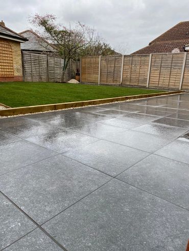 Wet patio tiles next to a green lawn and wooden fence on a cloudy day.