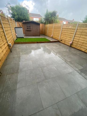 Backyard with wet tiled floor, small artificial grass patch, and wooden sheds.