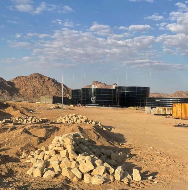 Industrial water tanks in a desert landscape under a partly cloudy sky.