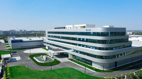Modern industrial building with glass facade and green surroundings.