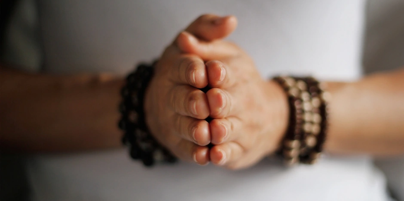 Hands clasped together in a prayer or meditation pose with beaded bracelets.