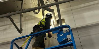 Worker in safety gear on a blue lift repairing ceiling pipes.