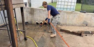 Worker cleaning an outdoor industrial area with a hose.