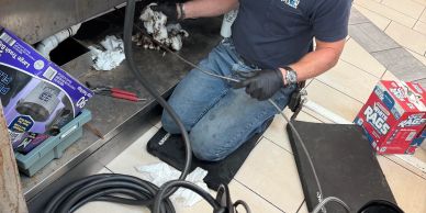 A technician repairs and cleans equipment with tools and cables on the floor.