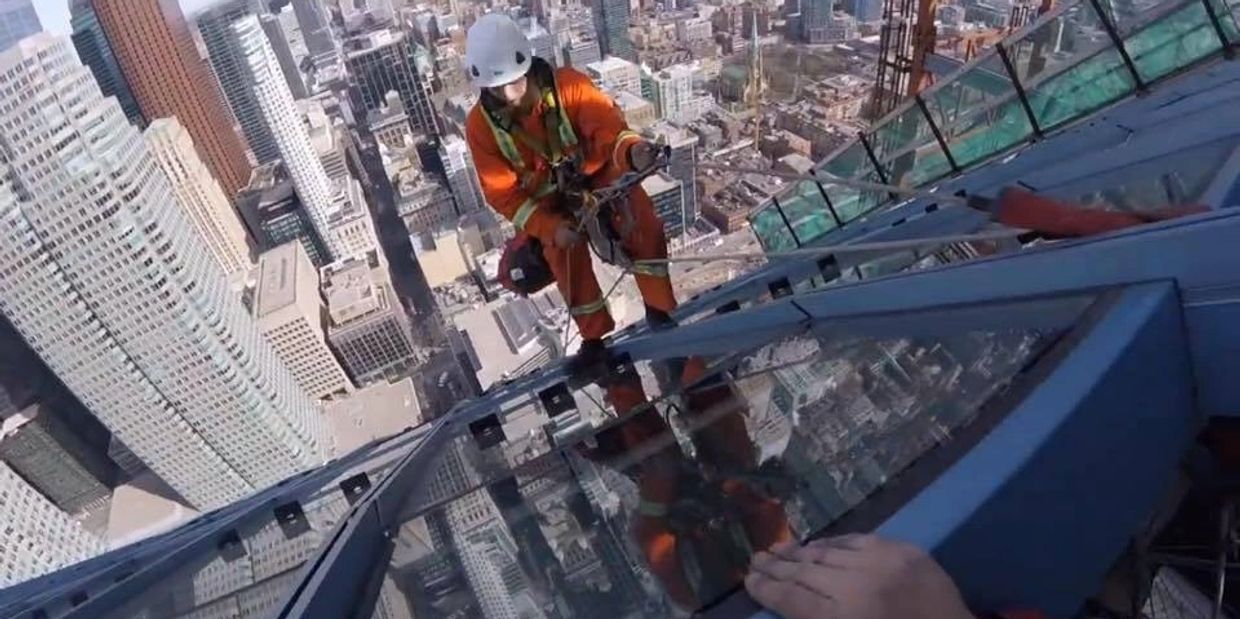 High-rise window cleaner in orange safety gear scaling a skyscraper, part of Skyline Canada’s professional exterior window cleaning services.