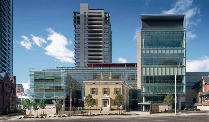 Modern glass buildings alongside a historic brick house under a blue sky.