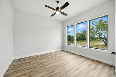 Empty room with wood flooring, large windows, and a ceiling fan.