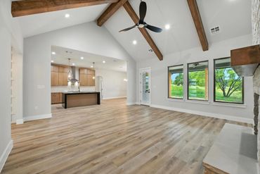 Spacious open-concept living area with vaulted ceilings and wooden beams.