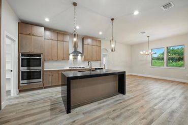 Modern kitchen with wooden cabinets and a large island under pendant lights.