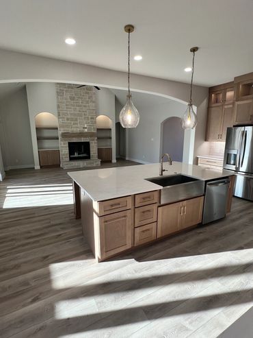 Modern kitchen with island, stone fireplace, and wooden floors.