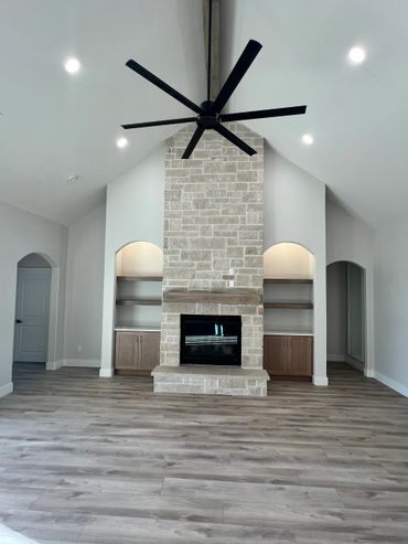 Modern living room with stone fireplace and high ceiling fan.