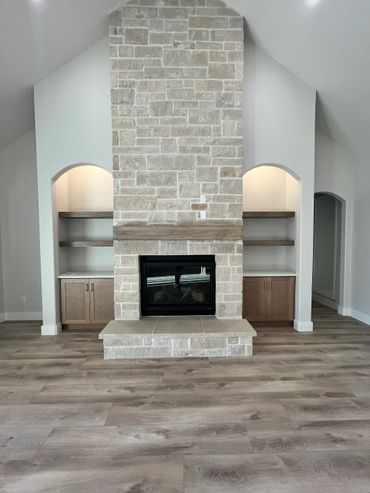 Modern stone fireplace with built-in shelves and wooden floor.
