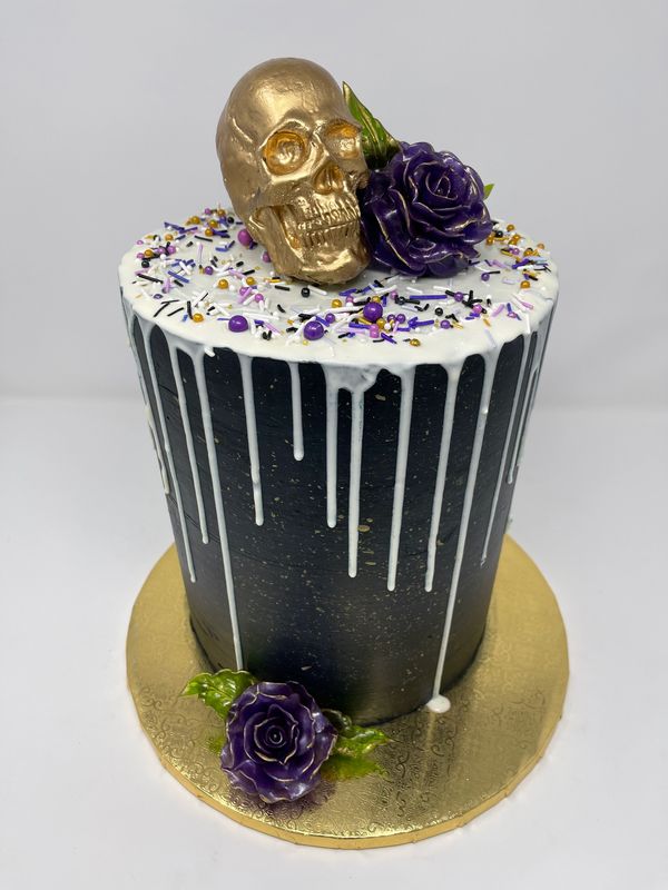 Black cake with white drip, gold skull and purple roses.