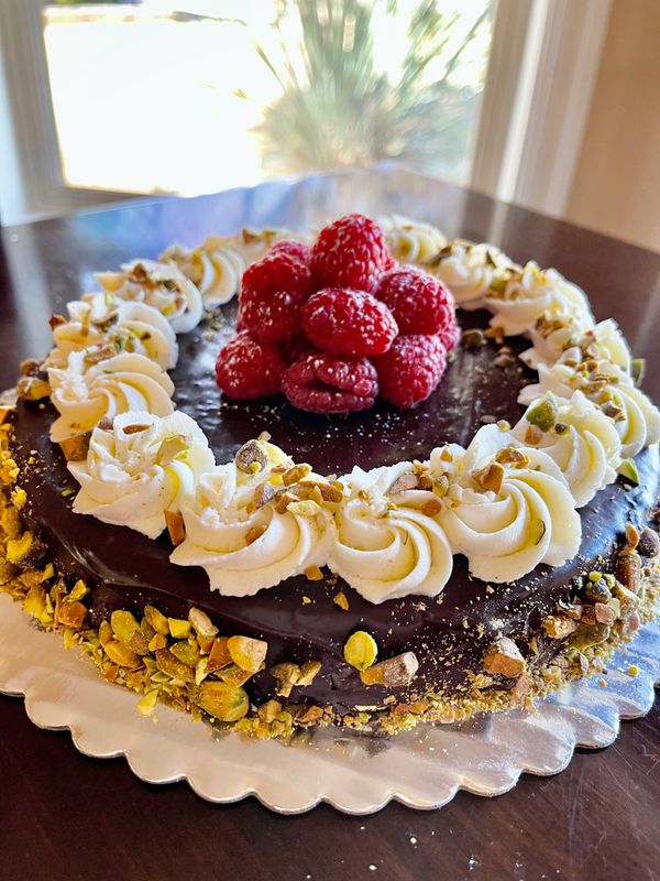 brown cake with white rosettes, red raspberries and pistachios