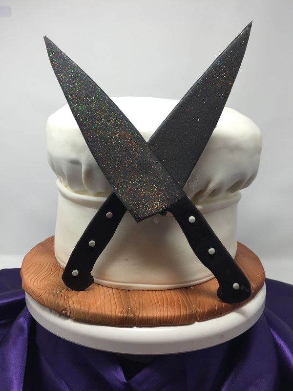white chef's hat cake with 2 knives crossed in front
