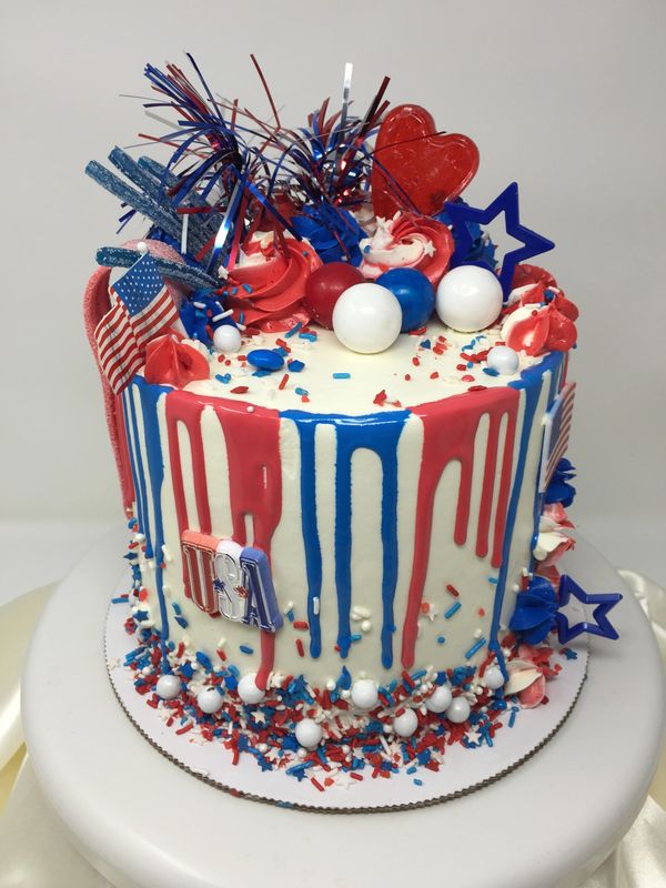 white cake with blue and red drip, flags, stars and gumballs on top