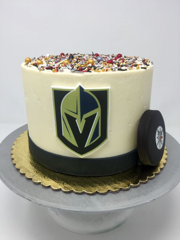 white cake with Vegas Gold Knights logo and hockey puck on the sides of the cak